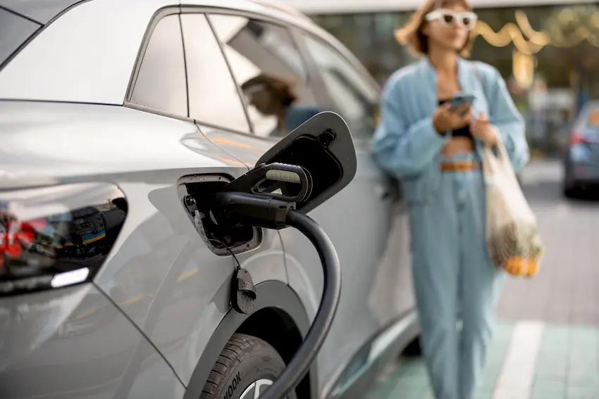 Mujer carga su coche eléctrico meintras espera